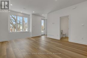 Ottawa multi-family for rent - A spacious room with wooden flooring and white walls, with a window showing a tree outside.