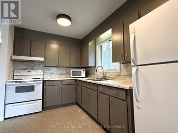 Fort Erie (Crescent Park) apartment for rent - A kitchen with a white fridge, white oven, and brown cabinets.