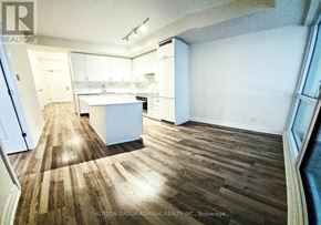 Vaughan (Concord) condo for rent - A room with wooden floors and white walls, with a kitchen area in the background.