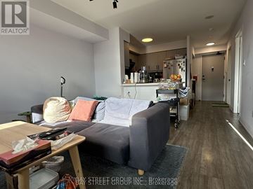 Richmond Hill (Langstaff) condo for rent - A living room with a grey couch and a kitchen area in the background.
