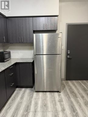 Waterloo condo for rent - A stainless steel refrigerator stands in a kitchen with dark wood cabinets.