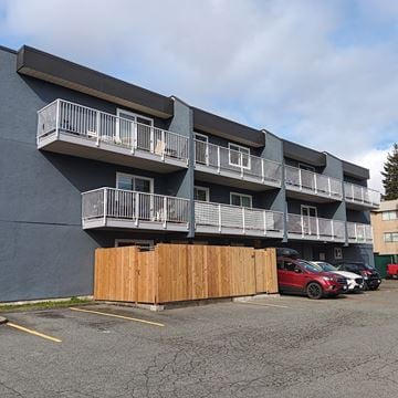 Nanaimo apartment for rent - A parking lot with a red car and a building with balconies.