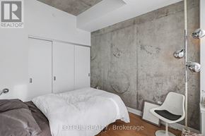 Ottawa condo for rent - A bedroom with a bed, chair, and a concrete wall.