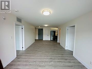 Windsor condo for rent - A spacious room with a door on the left and a kitchen area with a refrigerator and cabinets on the right.