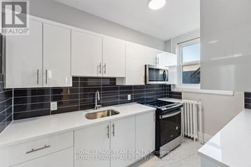 Ottawa apartment for rent - A modern kitchen with white cabinets and black appliances.