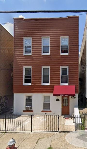 Jersey City apartment for rent - A brown building with a red awning is in front of a black fence.
