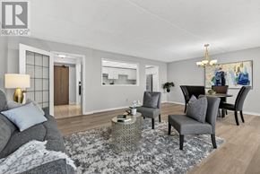 Hamilton (Stoney Creek) condo for rent - A living room with a grey couch, a grey armchair, a coffee table, and a chandelier.