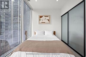 Toronto (Waterfront Communities) condo for rent - A bedroom with a large bed and a window overlooking a cityscape.