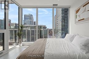 Toronto (Waterfront Communities) condo for rent - A bedroom with a large bed and a view of the cityscape outside the window.
