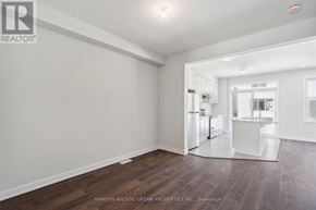 Ottawa townhouse for rent - A spacious room with wooden flooring and white walls, with a kitchen area visible in the background.