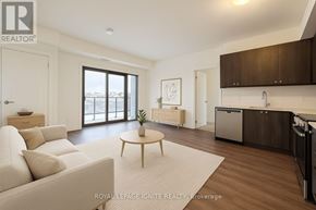 Clarington (Bowmanville) condo for rent - A well-lit, modern living room with a large window, a sofa, a coffee table, and a kitchen area in the background.