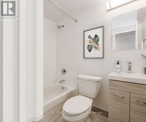 Toronto (Danforth Village-East York) condo for rent - A white toilet in a bathroom with a framed picture of leaves on the wall.