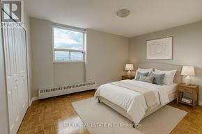 Toronto (Woburn) condo for rent - A bedroom with a large bed, a window with a view, and a wooden floor.