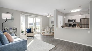 Farmington Hills apartment for rent - A well-lit living room with a grey sofa and a dining area in the background.