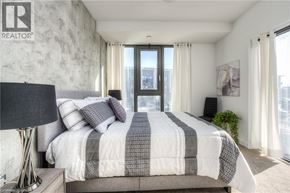Kitchener condo for rent - A bedroom with a large bed and a window overlooking a cityscape.