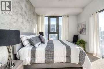 Kitchener condo for rent - A bedroom with a large bed and a window overlooking a cityscape.