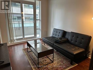 Toronto (University) condo for rent - A black sofa with tufted detailing sits in a living room with a glass coffee table in front of it.