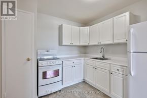 Port Hope condo for rent - A white kitchen with a stove, sink, and cabinets.