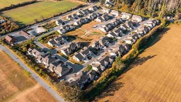 Saanichton apartment for rent - A bird's eye view of a residential area with houses surrounded by trees and grassy fields.