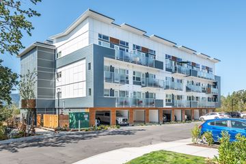 Brentwood Bay apartment for rent - A modern multi-story building with a parking lot in front.