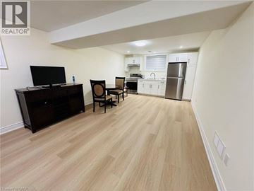 Niagara Falls apartment for rent - A living room with a television, chair, and a kitchen area in the background.