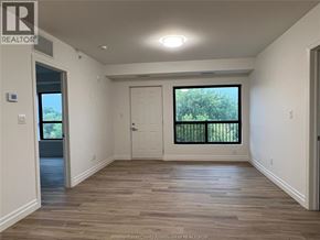 Windsor condo for rent - A spacious room with wooden flooring and a large window with a view of trees.