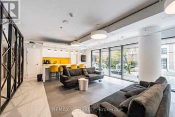 Toronto (Kensington-Chinatown) condo for rent - A modern living room with a grey couch and a yellow kitchen in the background.