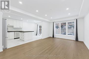 Brampton (Northwest Brampton) apartment for rent - A spacious room with wooden flooring and white walls, featuring a kitchen area with white cabinets and a window with a view of the city.