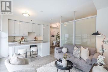Toronto (University) condo for rent - A modern living room with a grey couch and a kitchen area in the background.