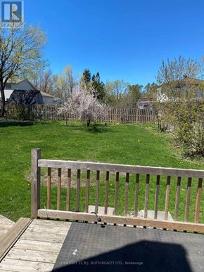 Barrie (Cundles East) apartment for rent - A wooden deck with a railing overlooks a green lawn and trees.