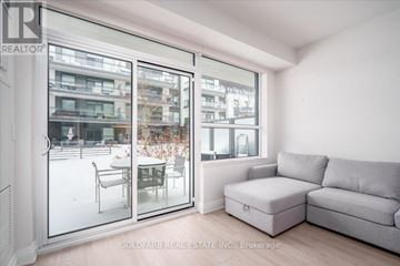 Innisfil condo for rent - A living room with a grey couch and a glass door leading to a balcony.