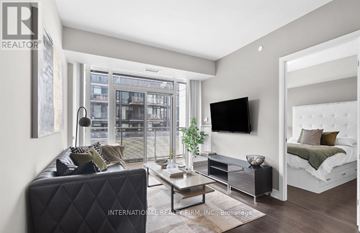 Toronto (Waterfront Communities) condo for rent - A modern living room with a black leather sofa and a flat screen TV mounted on the wall.