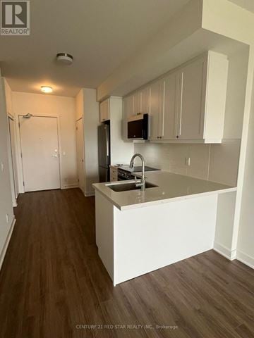 Clarington (Bowmanville) condo for rent - A kitchen with white cabinets and a wooden floor.