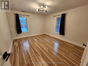 Windsor apartment for rent - A room with wooden flooring and two windows with black curtains.