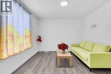 Windsor apartment for rent - A living room with a green couch, a wooden table with a vase of red flowers, and a window with a yellow and pink curtain.