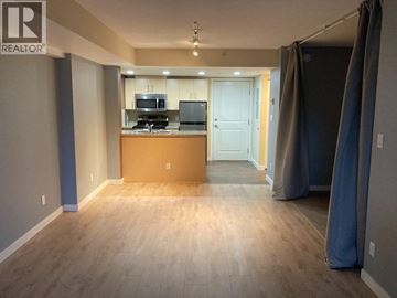 New Westminster apartment for rent - A room with a wooden floor and a kitchenette in the background.
