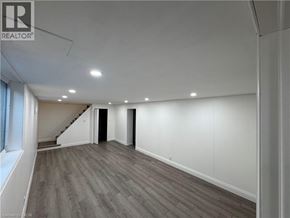 Kitchener apartment for rent - A spacious room with wooden flooring and a staircase leading to another level.