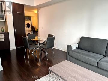 Toronto (Waterfront Communities) condo for rent - A grey couch sits in a living room with a coffee table and a dining table with chairs.