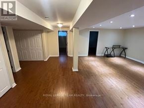 Ottawa apartment for rent - A spacious room with wooden flooring and white walls, with a door at the end of the hallway.