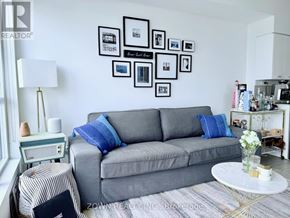 Toronto (Bayview Village) condo for rent - A grey couch with blue pillows sits in a living room with a white coffee table in front of it.