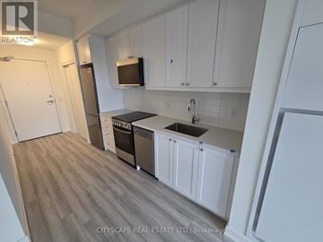 Clarington (Bowmanville) condo for rent - A kitchen with white cabinets and a wooden floor.