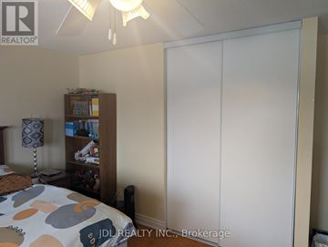Richmond Hill (Devonsleigh) apartment for rent - A bedroom with a bed, a nightstand with a lamp, a bookshelf, and a large white wardrobe.