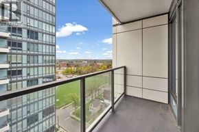 Kitchener condo for rent - A balcony with a glass railing overlooks a parking lot and buildings.