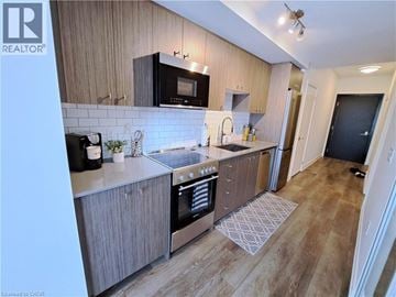 Kitchener condo for rent - A modern kitchen with wooden cabinets and a black microwave above the stove.