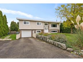 Chilliwack apartment for rent - A two-story house with a garage is surrounded by a well-maintained lawn and a stone wall.