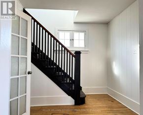 Cobourg apartment for rent - A white room with a wooden floor and a staircase with a black railing.