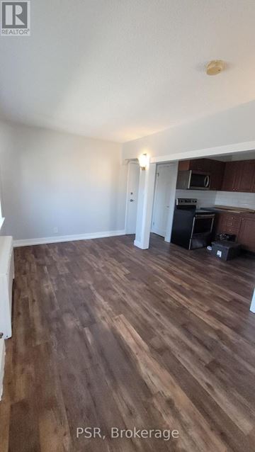 Toronto (Danforth Village-East York) apartment for rent - A room with wooden flooring and a kitchen area in the background.