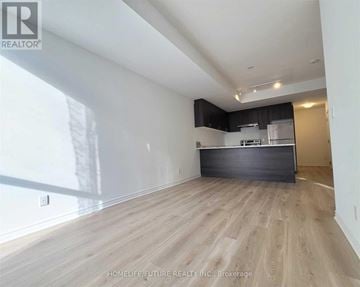 Toronto (West Hill) townhouse for rent - A spacious room with wooden flooring and a kitchen area in the background.