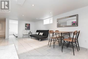 Toronto (Wychwood) apartment for rent - A living room with a black couch, a wooden table and chairs, and a large mirror on the wall.