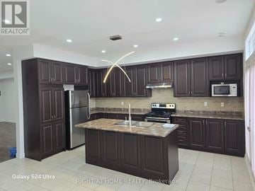 Brampton (Sandringham-Wellington North) townhouse for rent - A kitchen with dark brown cabinets and a granite countertop.